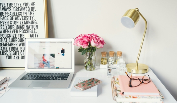 Image of a clean and tidy desk with lamp, laptop, phone, a print nad some roses